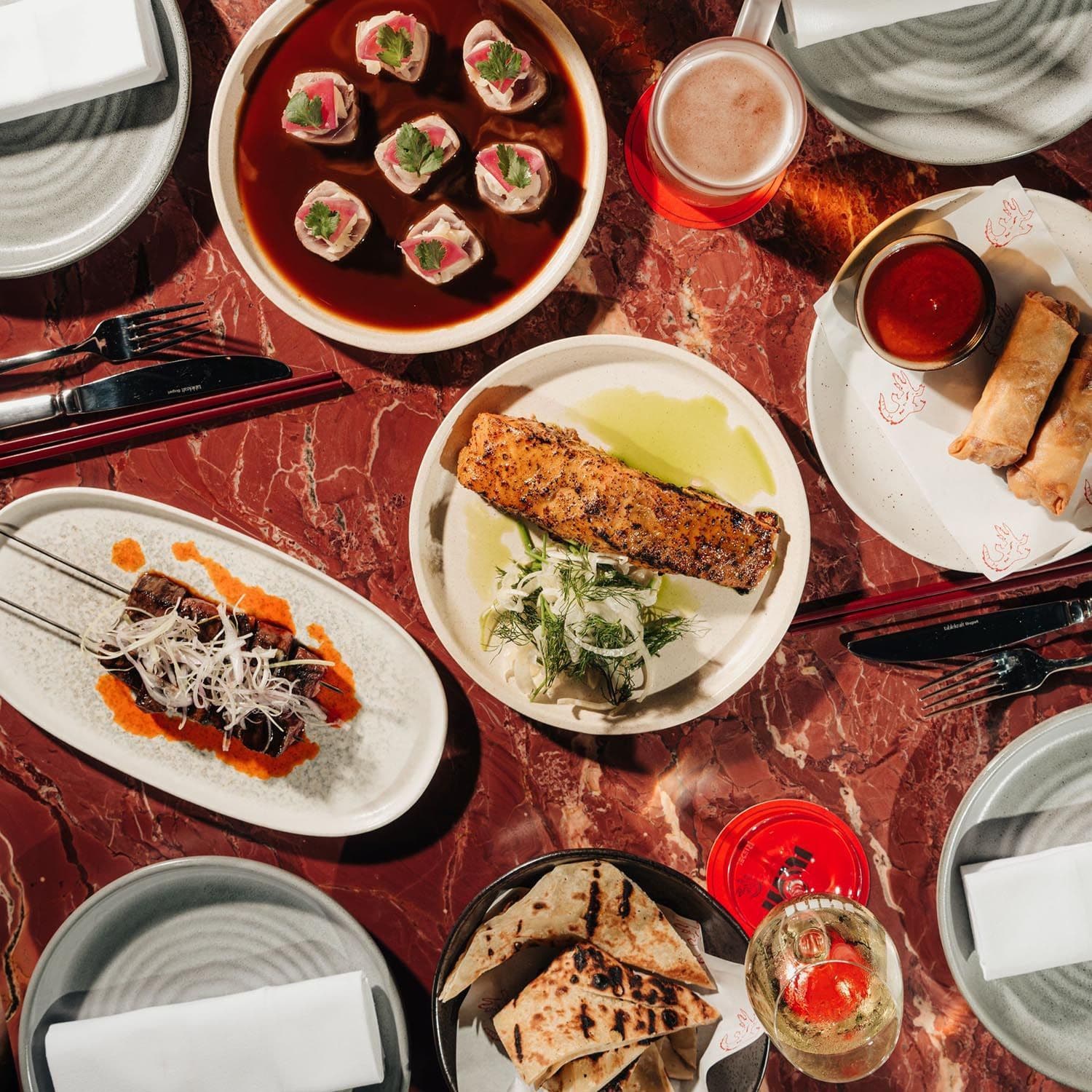 Assortment of gourmet dishes including fish, skewers, and dumplings on a red marbled table.