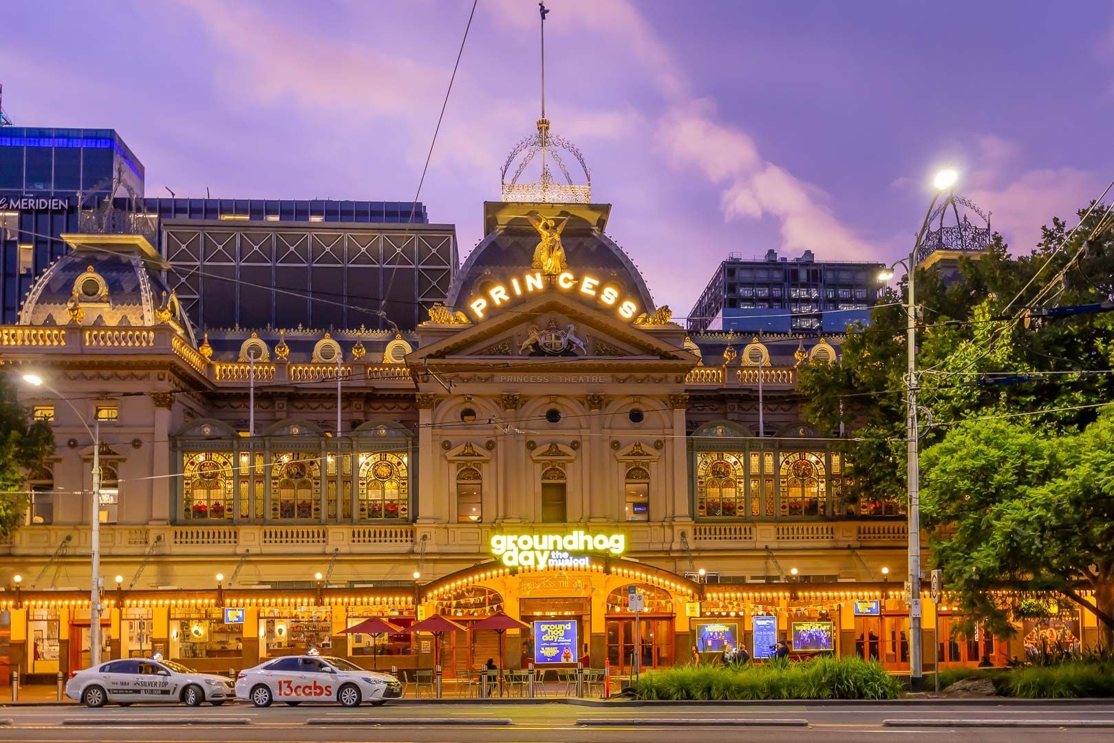 Grand historic building illuminated at dusk with cars on a city street.