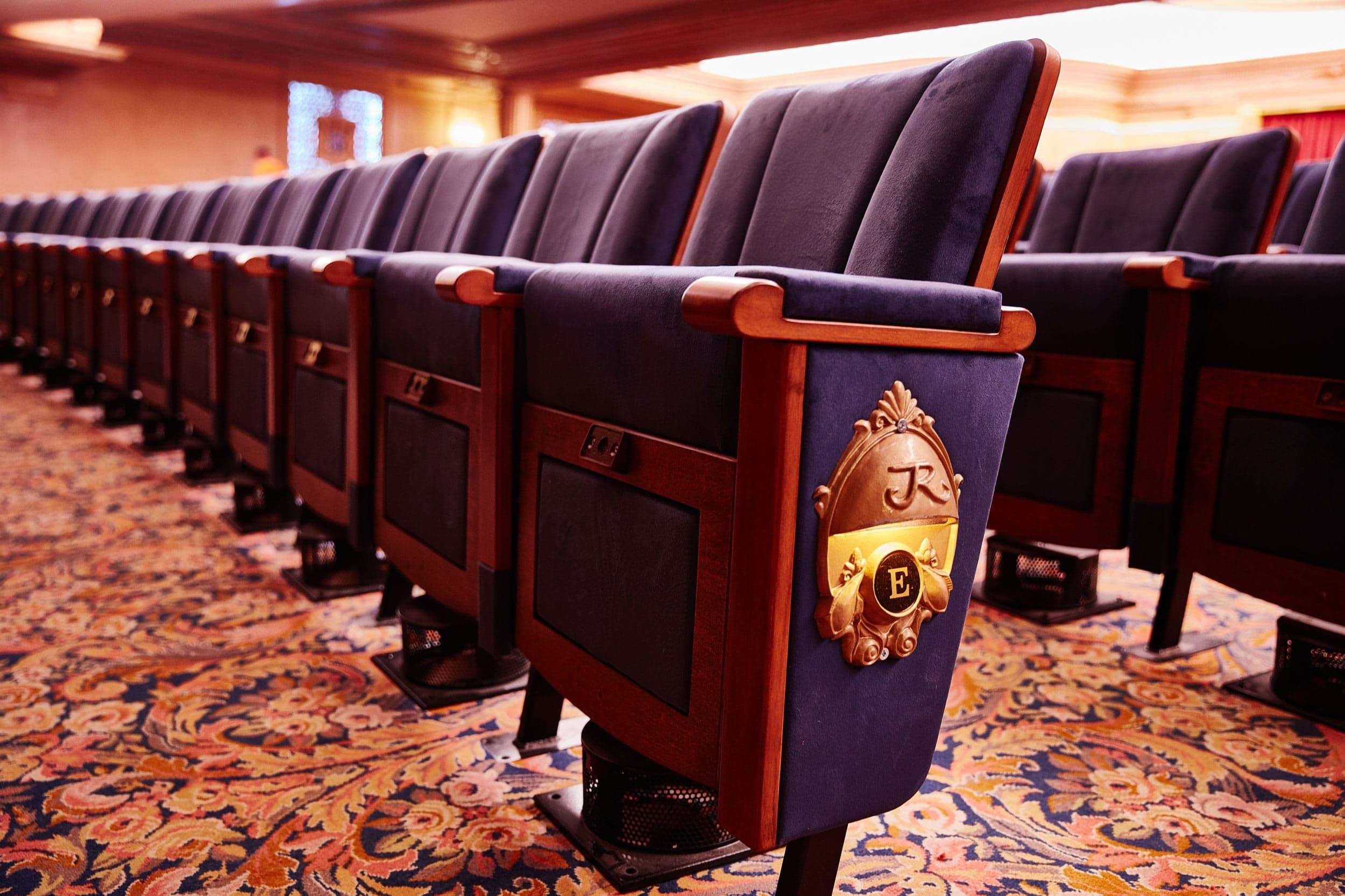 Close-up of elegant blue theater seats with wooden arms and golden embossed details.